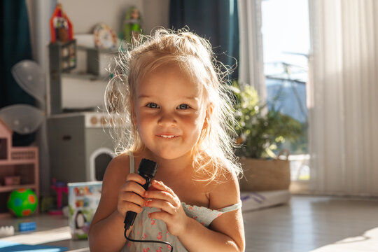 Toddler girl sings with toy microphone in bright room