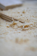 Close-up view of fine wood shavings scattered on a workbench, with blurred pages of a book in the background, showcasing craftsmanship and woodworking materials