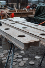 Wooden workbench with circular cutouts, surrounded by construction materials and tools, showcasing craftsmanship and industrial workspace atmosphere in a busy workshop environment