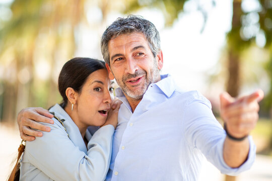 Excited woman and smiling man pointing at something surprising outdoors