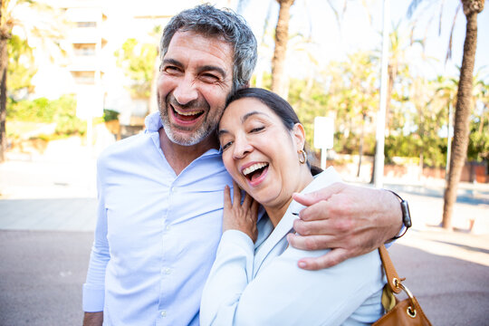 Joyful middle-aged couple laughing and embracing on a city street