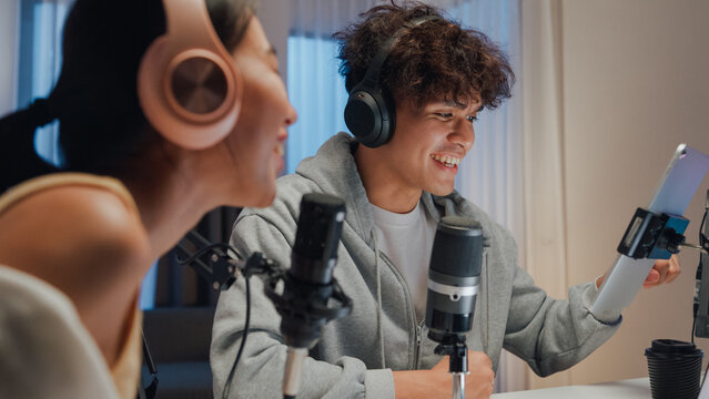 Close-up Young happy Asia couple wear headphone sit on desk online live streaming football live score watch soccer sport game on laptop use microphone talk with follower small studio in home at night.
