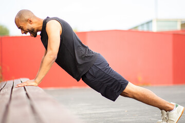 Fototapeta premium Screaming man with shaved head and beard exercising outdoors doing push-ups on bench
