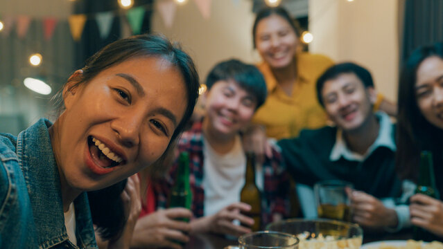 Closeup Group of diversity adult Asia people use phone greeting friend on remote video call hangout party at dining table in night life indoor home. Happy hour millennial generation inside house.