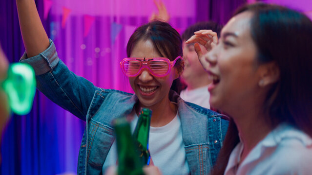 Closeup group multiethnic young adult Asia friend wear futuristic neon glowing glasses dance and drink alcohol beer fun hangout party in living room night indoor home. Disco lights illuminating house.