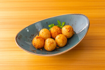 Eight steaming pieces of takoyaki garnished with green aonori seaweed and sweet sauce on a bamboo plate