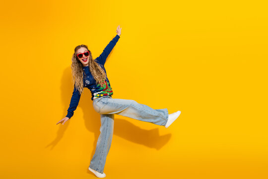 Joyful young woman dancing in festive sweater on vibrant yellow background, celebrating holiday season and Christmas magic