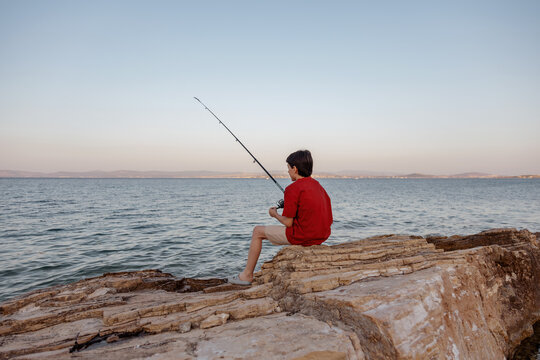 Boy fishing on rocky shoreline at serene seascape
