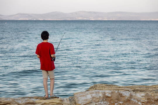 Boy fishing on rocky shore by the sea