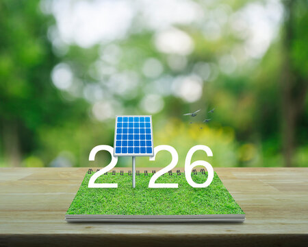 2026 white text with solar cell on green grass on open book on wooden table over blur tree in park, Happy new year 2026 ecological cover concept