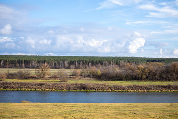 River landscape with green field, forest line and cloudy sky. Nature, rural scenery, environmental background. Autumn. Real photo