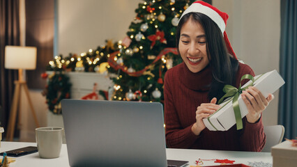 Attractive Asia female blogger new normal shopping online christmas gift unbox review celebrate christmas video conference call with follower on computer laptop in social media platform at house.