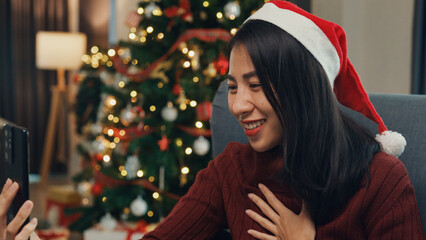 Happy Asia girl wear red santa hat new normal celebrate christmas party at home with smartphone...
