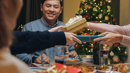 Group of Asia colleague friends gathering New year holidays party together. Group happy of friends laughing and sharing gifts on christmas dinner at home in evening, celebration and people concept.