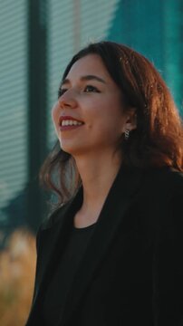 Young professional woman walking confidently through a modern city street, smiling and enjoying sunny afternoon, stylish and poised against sleek urban office architecture