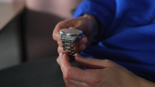 A man in a blue sweater holds a metal wristwatch with a metal strap.
The man is checking the functionality of his watch.
Watch, time, accessory, luxury, hour, minutes