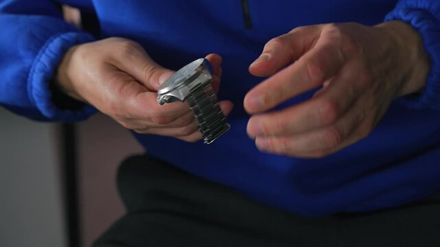 A man in a blue sweater holds a metal wristwatch with a metal strap.
The man is checking the functionality of his watch.
Watch, time, accessory, luxury, hour, minutes