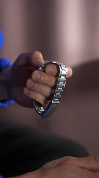 A man in a blue sweater holds a metal wristwatch with a metal strap.
The man is checking the functionality of his watch.
Watch, time, accessory, luxury, hour, minutes