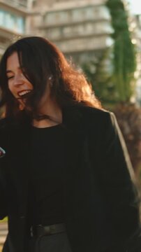 Ecstatic young woman receiving amazing news on her smartphone, celebrating with a joyful dance in a city park at sunset, expressing pure happiness and success with a radiant smile