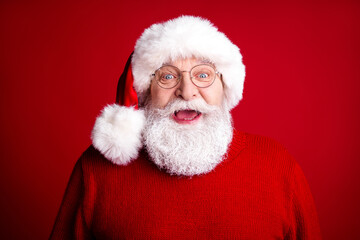 Santa Claus in a fluffy white hat and red sweater smiles warmly against a bold red background creating a festive Christmas mood