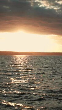 Beautiful golden sunset light reflecting on the calm sea surface with gentle waves, creating a serene and peaceful atmosphere with a distant shoreline visible under a cloudy sky