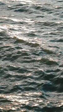Dark sea water surface sparkling and waving in the sun with golden reflections during a beautiful and tranquil sunset, creating a relaxing and meditative background with gentle movement