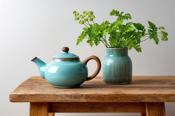 A teal ceramic teapot and a vase with green foliage sit on a rustic wooden table
