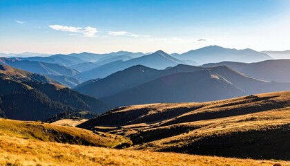 A vast landscape of rolling mountain ranges under a clear blue sky, with foreground slopes covered in golden dry grass.