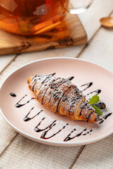 Freshly baked croissant topped with chocolate drizzle and powdered sugar served on a pink plate
