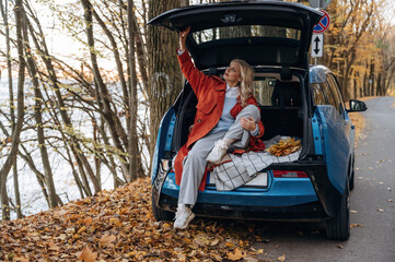 Enjoying the nature, relaxing. Beautiful blonde woman is with her blue electric car on the road of forest
