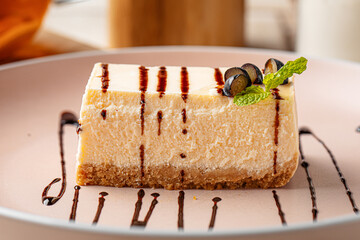 Creamy cheesecake slice with chocolate drizzle, fresh grapes and mint served on a pink plate