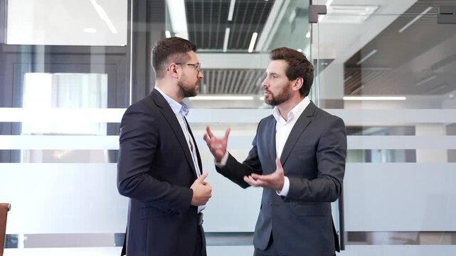 Two angry businessmen arguing intensely in modern office setting, showcasing conflict and emotion during heated business discussion or disagreement. Colleagues aggressive fight, disputing, quarreling
