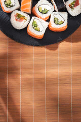 Philadelphia sushi roll salmon on round slate board and bamboo mat in soft sunlight.