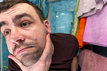 A young man scratches his unshaven beard in front of a mirror