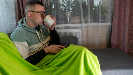 Young man sitting on the couch drinking tea from a cup