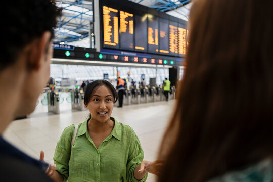 Friends having a conversation at a train station under the departure board