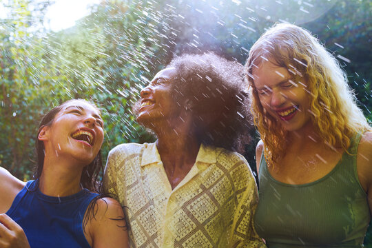 Friends laughing and enjoying a refreshing water splash in summer garden