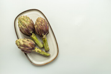 Tree heads of purple artichokes on a plate top view. Vegetables food ready to cook