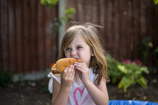 Child eating hot dog outdoors in summer garden barbecue party