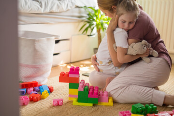 Mother comforting girl on floor with colorful blocks and stuffed animal
