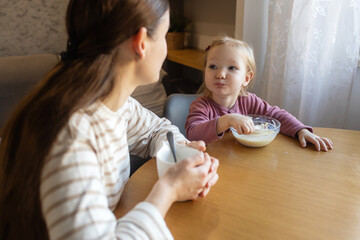 Happy single mother doing her daughter's hair while having breakfast. Woman combs the hair of a little girl. The concept of morning routine, single parenthood and preparation for school