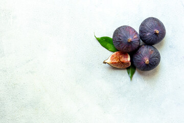 Purple ripe figs fruit and slices with green leaves top view on a stone background