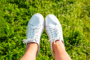 The legs of a girl in white sneakers on green grass. Sports shoes. Sunny summer bright day concept.