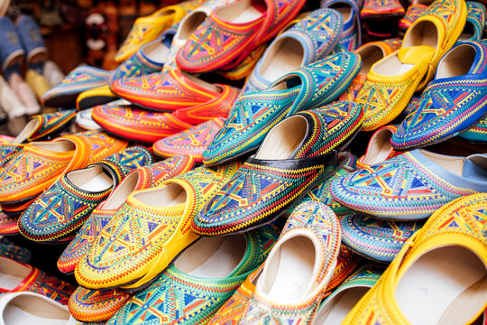 Colorful handmade shoes with intricate patterns are stacked together, showcasing vibrant designs and craftsmanship, representing cultural artistry and traditional footwear