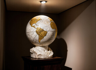 Illuminated globe on marble bust stand in corner with shadow against neutral color wall background