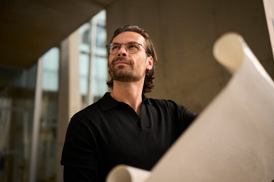 Confident architect planning with blueprint in modern urban workspace