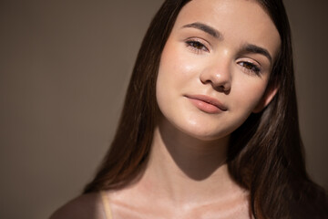 Obraz premium Young woman with long brown hair, softly lit against a neutral background, showcasing natural beauty and serene expression, embodying confidence and youthfulness in a portrait
