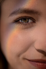 Close-up portrait of a young woman with a subtle rainbow reflection on her cheek, showcasing her bright eyes and soft smile, capturing a moment of serenity and beauty