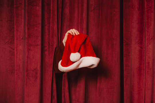 Hand holding Santa Claus hat in front of red velvet festive curtain