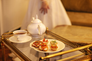 Elegant tea set with white teapot and cup, accompanied by assorted pastries on a glass table, creating a sophisticated afternoon tea atmosphere with inviting ambiance
